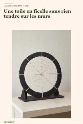 Anneau noir portant une toile en ficelle écrue à huit rayons et une spirale, posé sur un socle plat avec deux renforts triangulaires visibles sur les côtés.